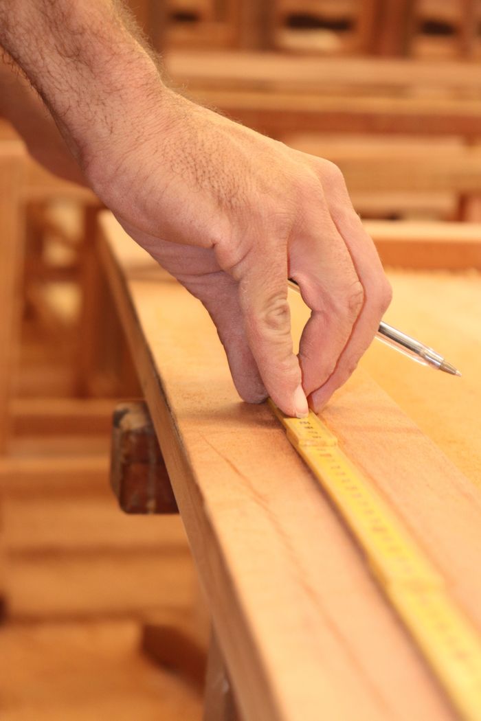 about-03 A craftsman carefully measures a wooden plank using a tape measure, showcasing woodworking precision.